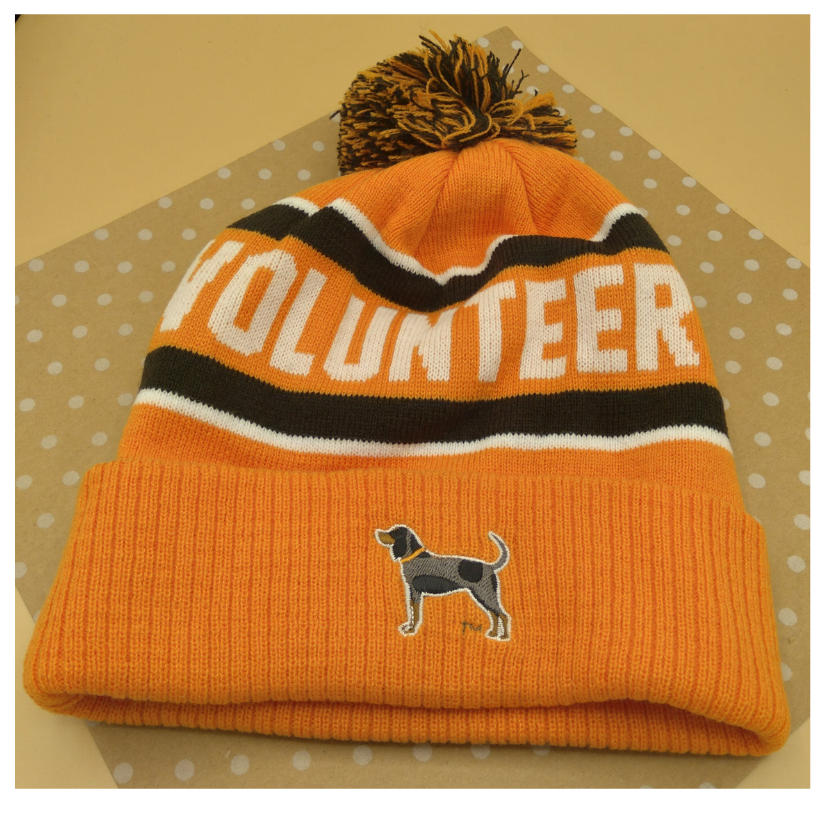 Orange beanie with 'VOLUNTEER' text and a logo on a beige background